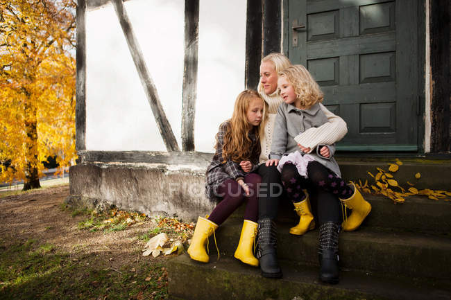 Madre e hijas sentadas al aire libre - foto de stock