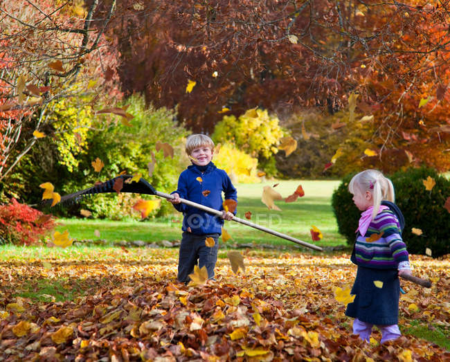 Niños rastrillando hojas de otoño - foto de stock