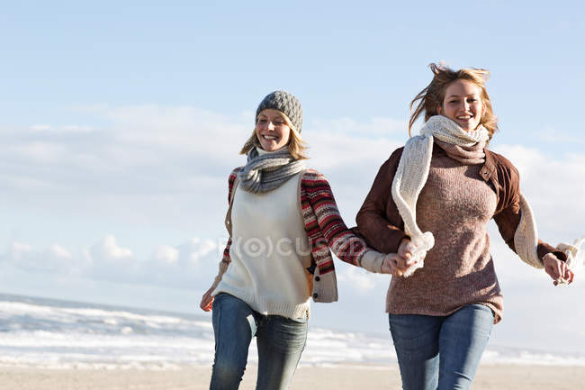 Mujeres sonrientes corriendo en la playa - foto de stock