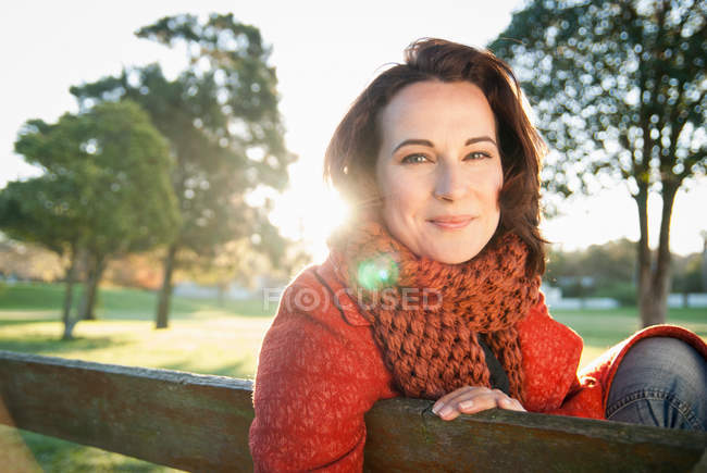 Mujer sonriente sentada en el banco del parque - foto de stock