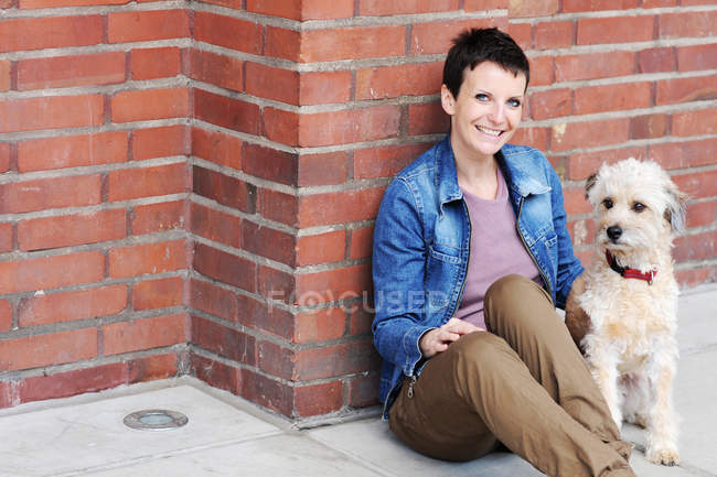 Woman and dog sitting on city street — Stock Photo