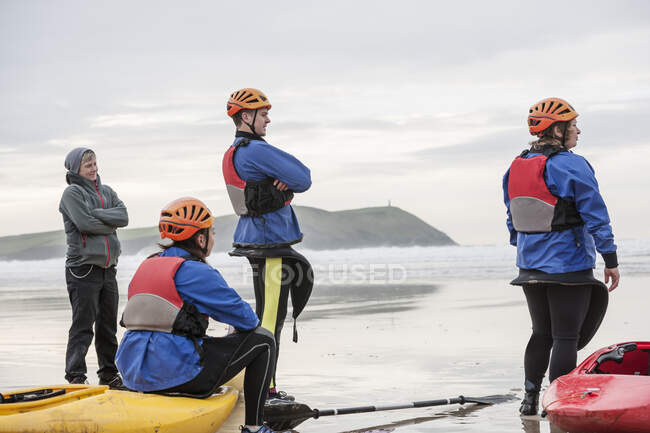 Vier Personen am Strand mit Kajaks, Polzeath, Cornwall, England — Stockfoto
