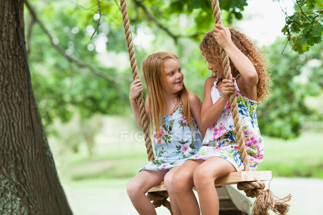 Smiling girls sitting in tree swing — Stock Photo
