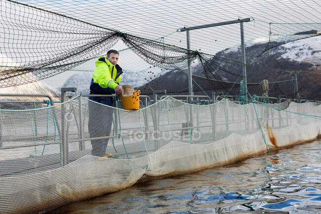 Trabajador en granja de salmón en lago rural - foto de stock