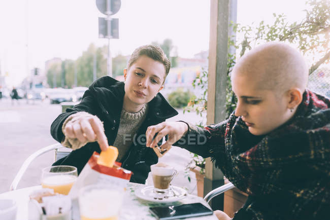 Two you female friends eating snack at sidewalk cafe — Stock Photo