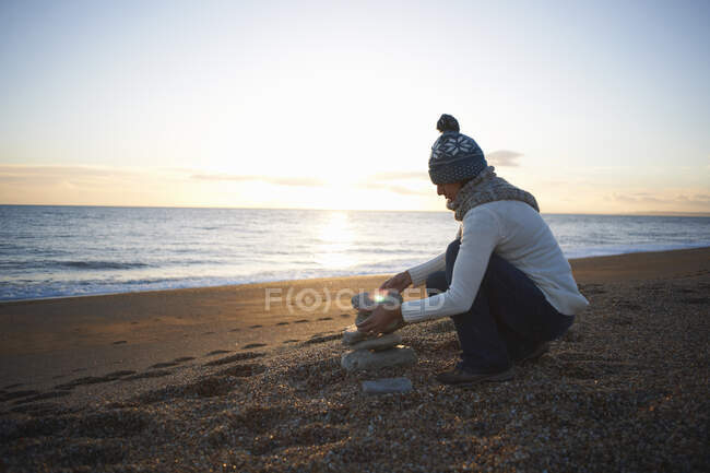 Femme mûre empilant des pierres sur la plage au crépuscule — Photo de stock