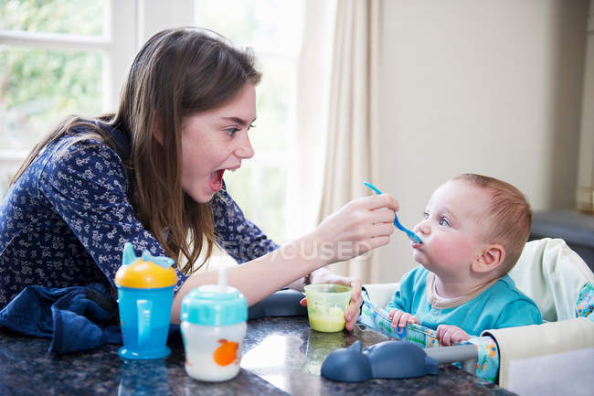 Menina alimentando bebê irmão à mesa — Fotografia de Stock