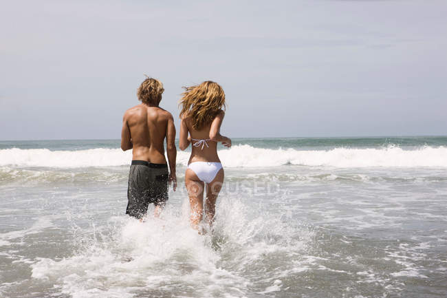Парень и девушка бегают в воде по пляжу — стоковое фото