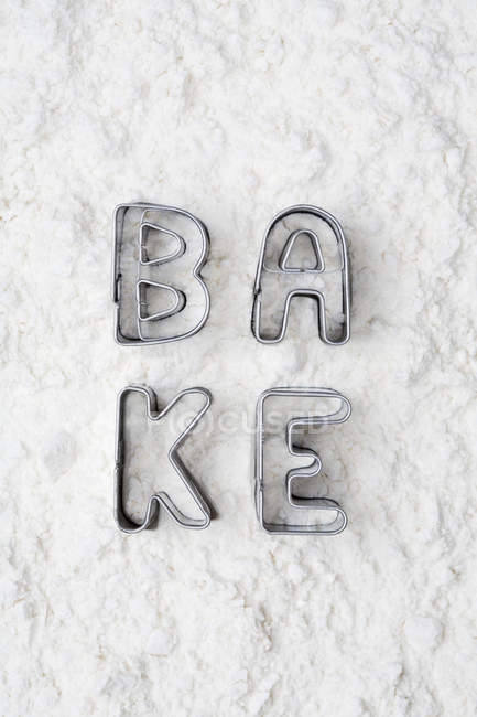 Cookie cutters spelling bake in flour — Stock Photo