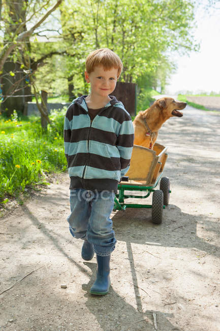 Garçon tirant chariot avec chien — Photo de stock