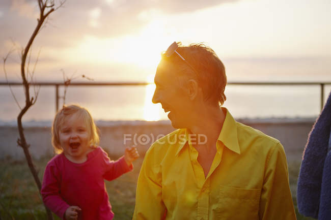 Padre e hija riendo en la costa soleada - foto de stock
