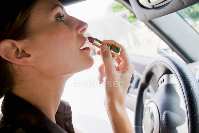 Женщина, использующая помаду в автомобильном зеркале — стоковое фото