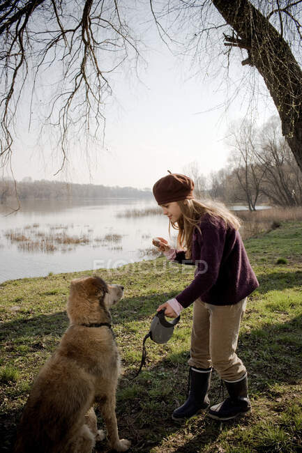 Fille par rivière tenant gâteau avec chien — Photo de stock