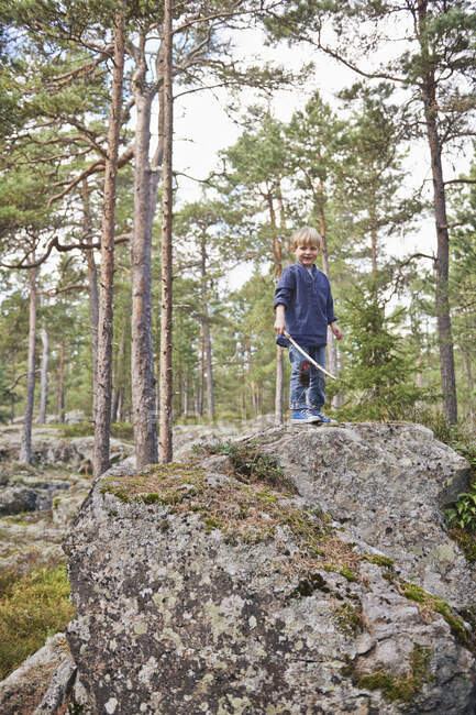 Boy standing on rocks holding stick — Stock Photo