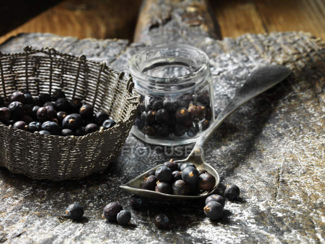Juniper berries in small glass jar, metal vintage spoon and woven basket — Stock Photo