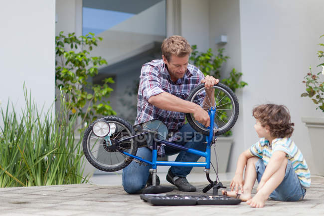 Pai ajudando filho corrigir bicicleta, foco seletivo — Fotografia de Stock
