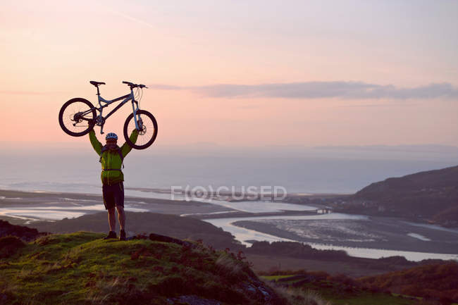 Hombre sosteniendo bicicleta en la colina - foto de stock