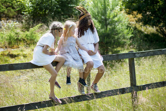 Girls in costumes sitting on fence — Stock Photo