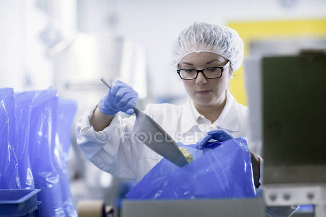 Factory worker scooping food into blue plastic bags — Stock Photo