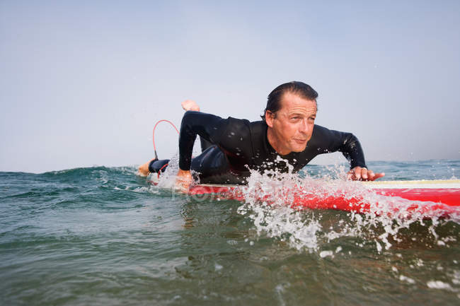 Людина лежить на дошці для серфінгу у воді — стокове фото