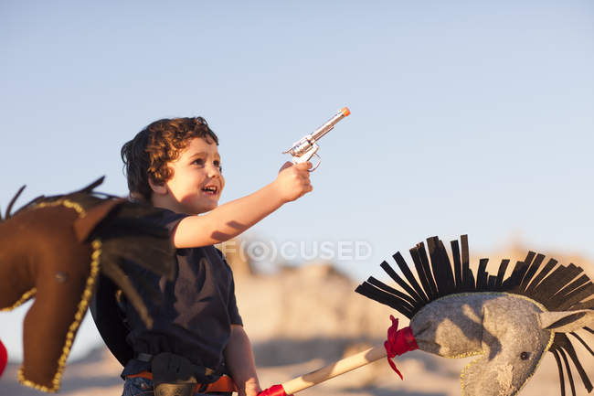 Menino vestido de cowboy com cavalo de passatempo e arma de brinquedo em dunas de areia — Fotografia de Stock