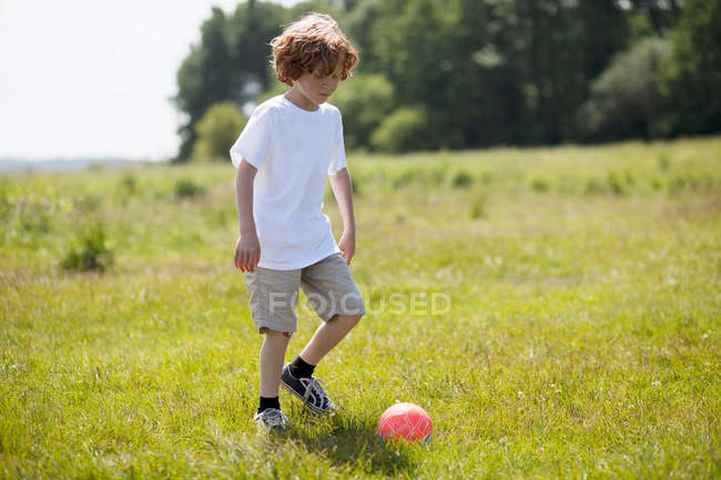 Boy kicking soccer ball in field — Stock Photo