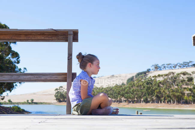 Mädchen sitzt auf Seebrücke, Seitenansicht — Stockfoto