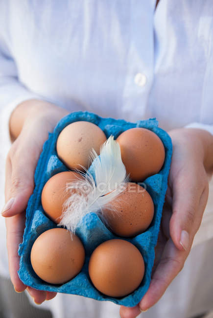 Woman holding eggs in box with feather — Stock Photo