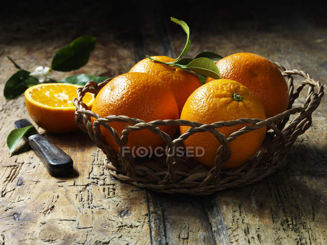 Arance in cesto con uno dimezzato su tavolo in legno rustico — Foto stock