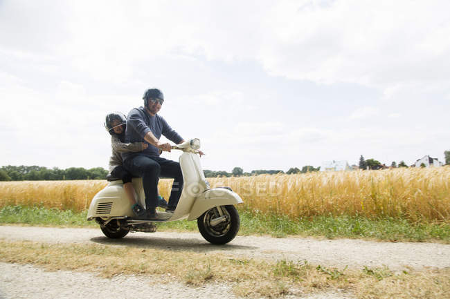 Зрелый мужчина и дочь едут на мотороллере по грунтовой дорожке — стоковое фото