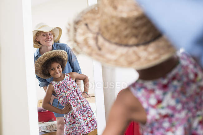 Mother and daughter looking in mirror while wearing sunhats — Stock Photo