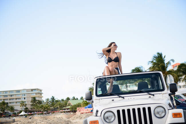 Woman sitting on roof of jeep on beach — Stock Photo