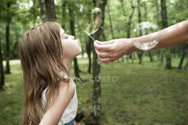Woman holding bubble wand, girl blowing bubble — Stock Photo