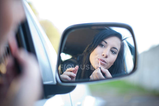 Young woman applying lipstick in car mirror — Stock Photo