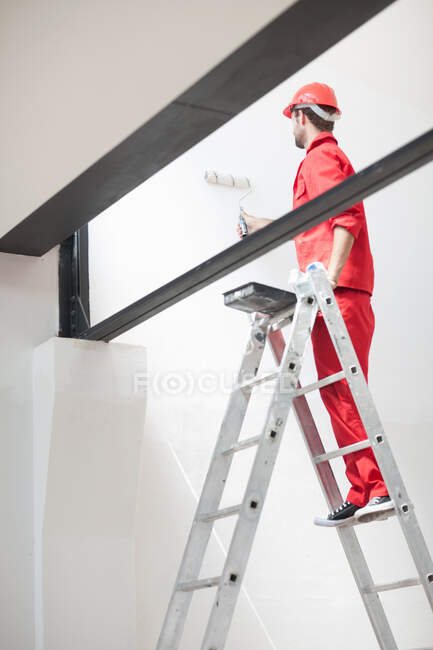 Decorator on ladder painting interior wall — Stock Photo