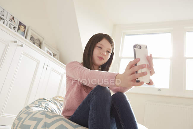 Chica sentada en una silla beanbag tomando selfie smartphone - foto de stock