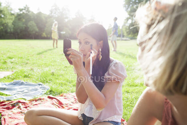 Amigas aplicando maquillaje en la fiesta del parque - foto de stock