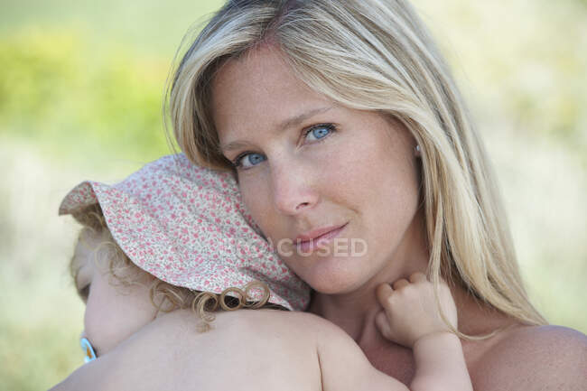 Mother hugging toddler wearing sunhat — Stock Photo