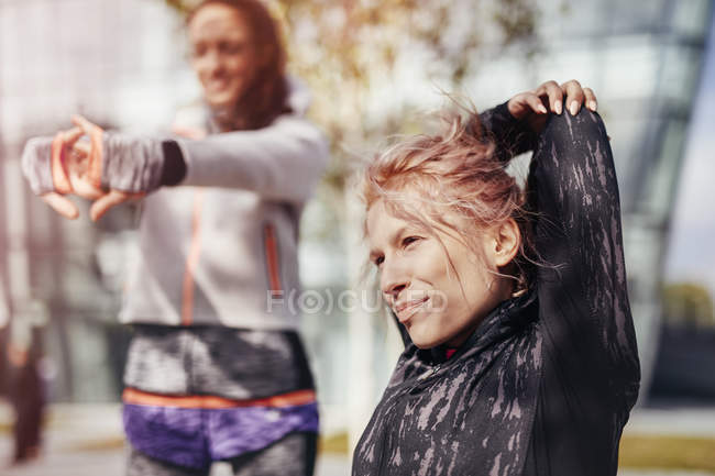 Дві жінки-бігуни, що розтягують руки в місті — стокове фото