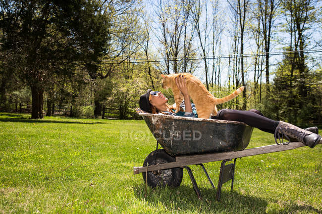 Woman in wheelbarrow holding ginger cat — Stock Photo