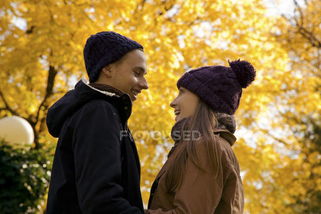 Pareja joven sonriendo cara a cara en el parque de otoño - foto de stock
