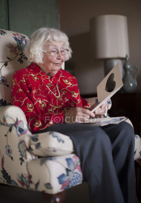 Senior woman sitting in chair, looking at greeting card — Stock Photo