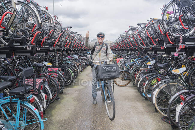 Цикліст на велосипеді дивиться на камеру, яка піднімає пальці вгору, Амстердам, Нідерланди. — стокове фото