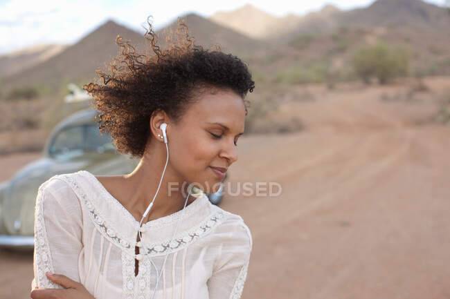 Young woman wearing earphones in desert on road trip, smiling — Stock Photo