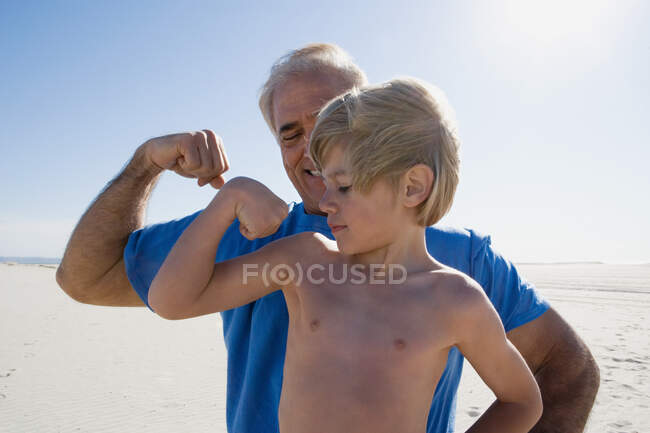 Grandfather and grandson flexing biceps on beach — Stock Photo