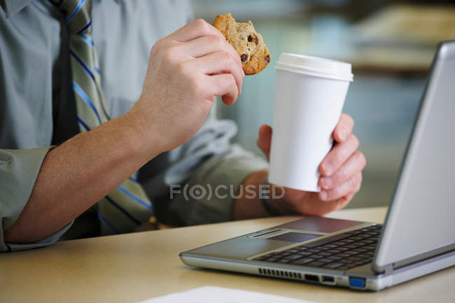 Uomo alla scrivania con caffè e biscotti — Foto stock