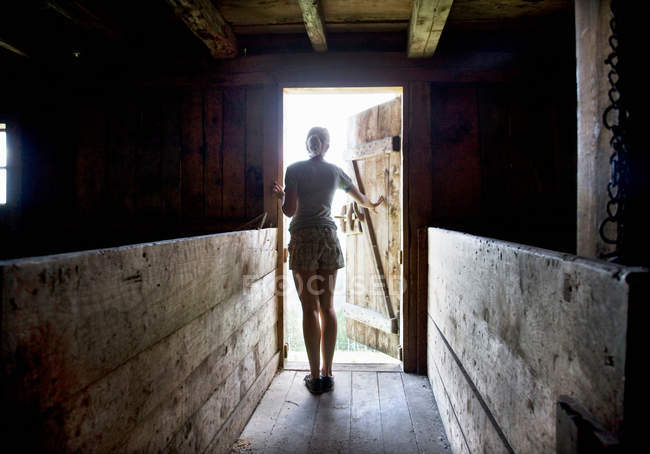 Visão traseira da menina olhando para fora da porta do celeiro — Fotografia de Stock