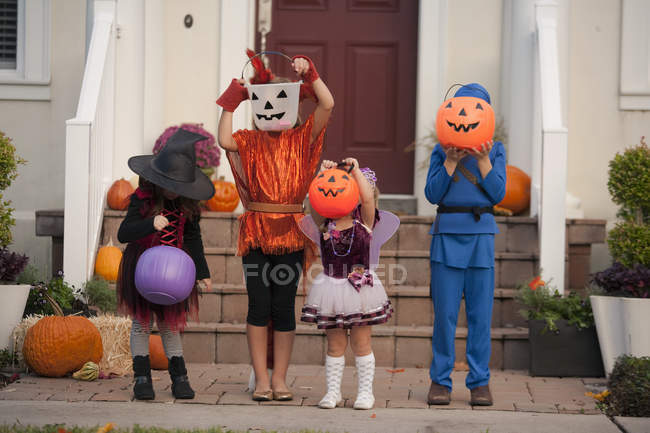 Children covering face with Jack O' Lantern bucket in front of house — Stock Photo