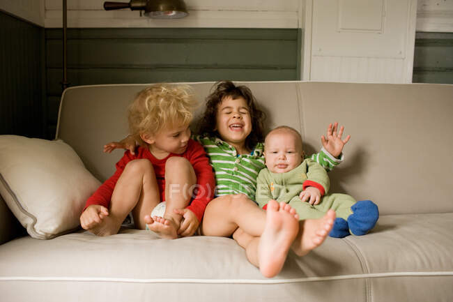 Три брата и сестры сидят на диване — стоковое фото