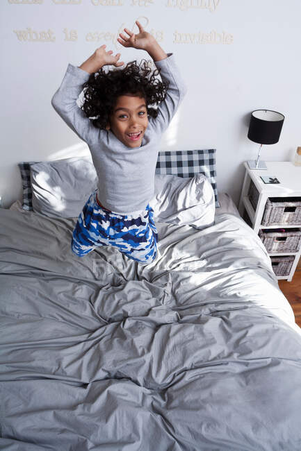 Menino pulando na cama com os braços para cima — Fotografia de Stock